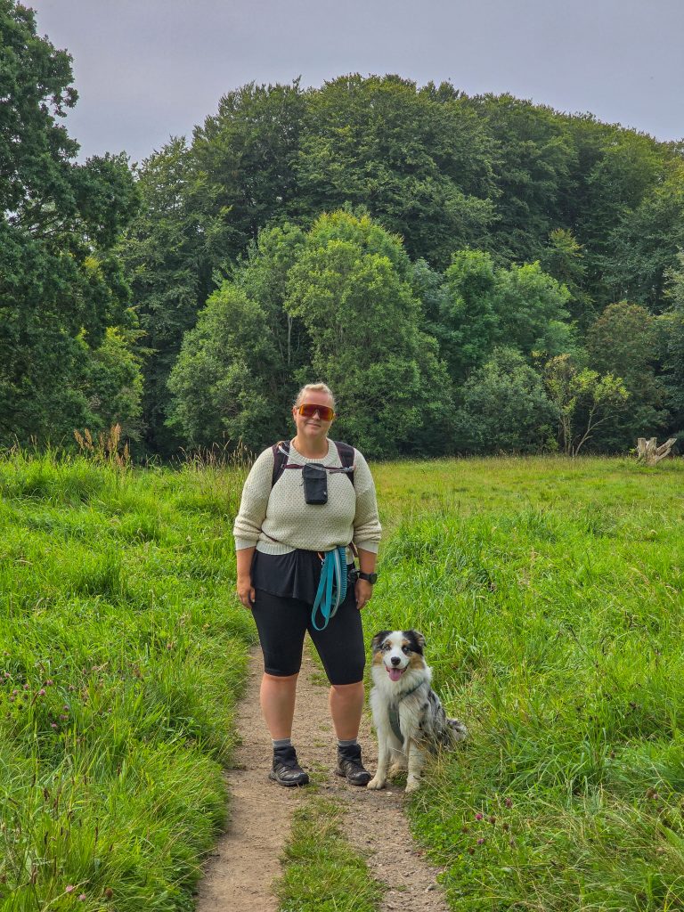 Woman hiking with her Australian Shepherd on a green countryside trail in Denmark.
