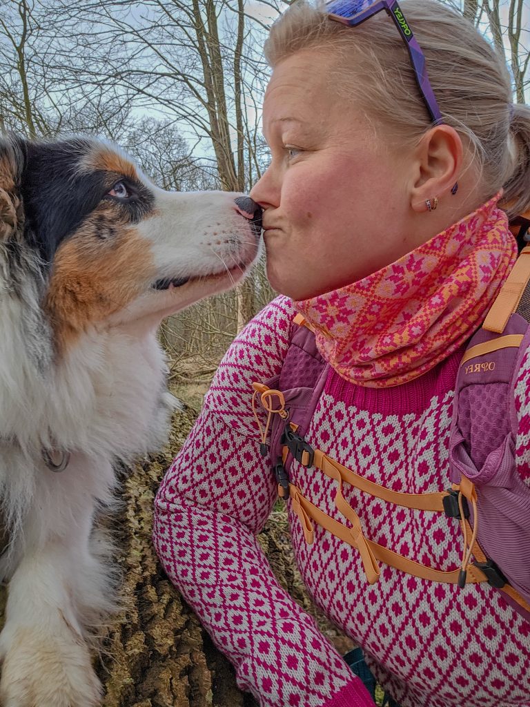 Woman sharing a playful nose-to-nose moment with her Australian Shepherd during a hike in the woods.