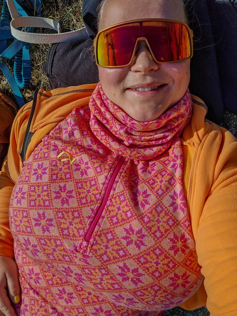 Woman resting outdoors in colourful pink and orange base layers and fleece after hiking.