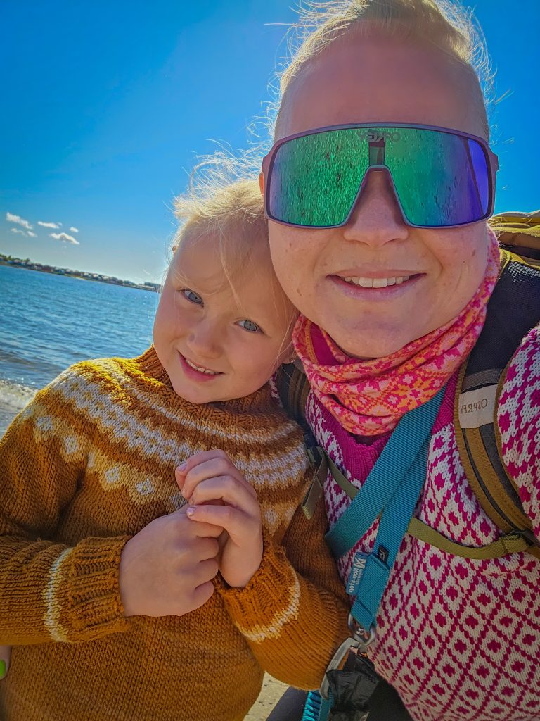 Woman and young girl smiling together during a sunny coastal hike by the sea.
