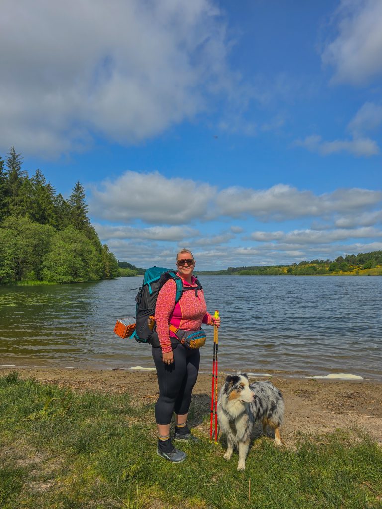 Plus-size woman hiking with a backpack and her dog by a lake in Denmark.