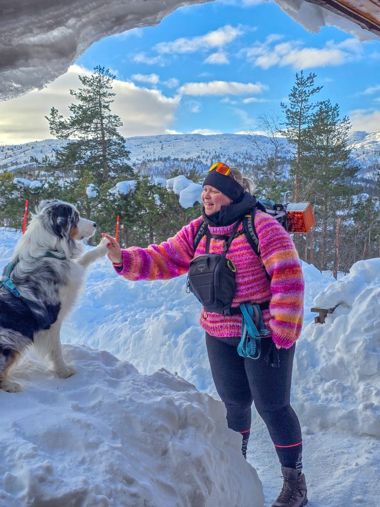 Woman winter hiking with her Australian Shepherd in a snowy mountain landscape.