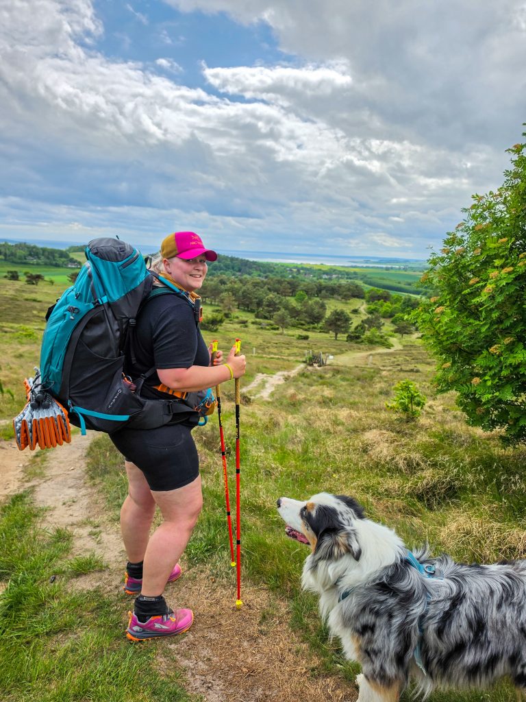 Woman backpacking with her Australian Shepherd on a scenic hiking trail in Denmark.