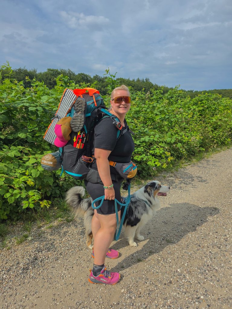 Woman hiking with a fully loaded backpack and her dog on a summer trail in Denmark.