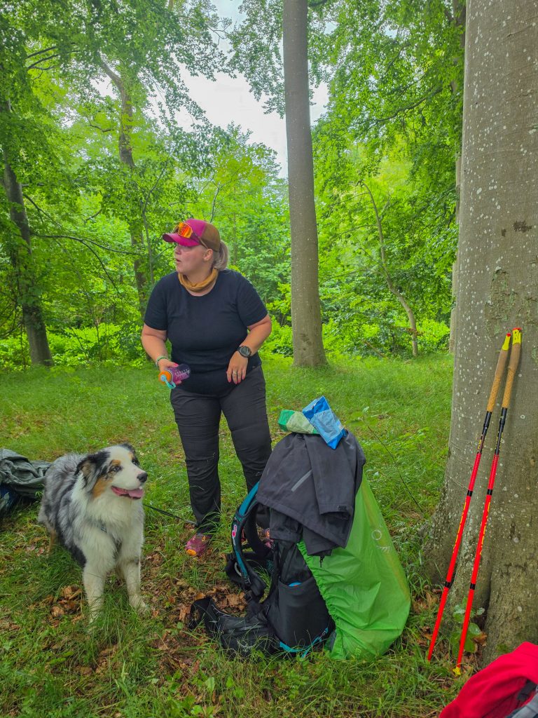 Woman taking a break with her dog and hiking gear during a backpacking trip in Denmark.