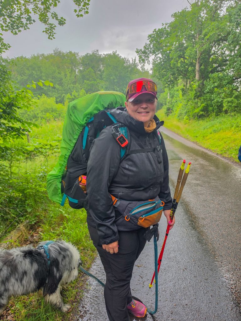Woman hiking with a fully loaded backpack and trekking poles on a rainy trail in Denmark.