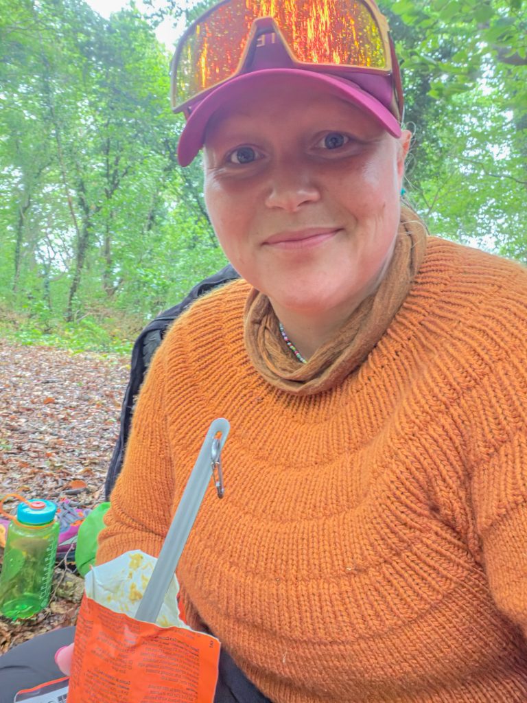 Woman enjoying a warm meal during a backpacking break in the forest.