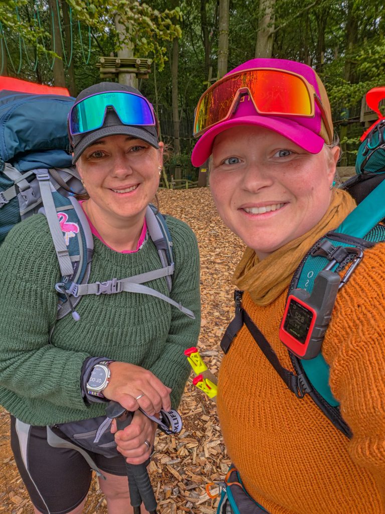 Two women smiling together with backpacks and hiking gear during an outdoor adventure.
