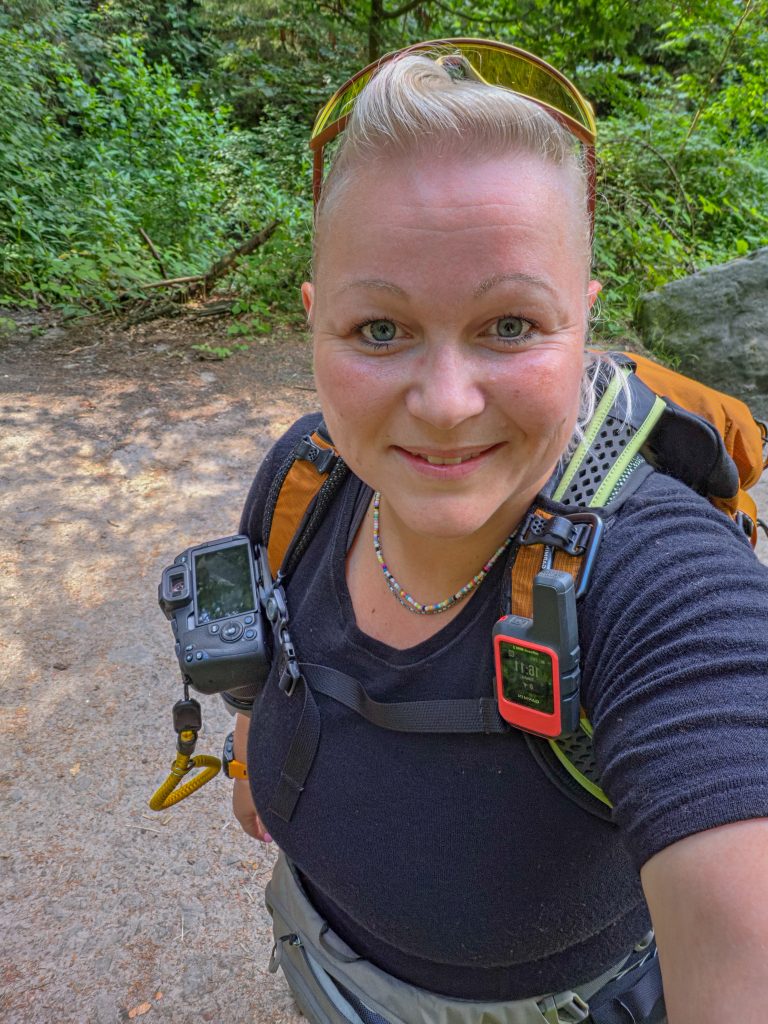 Woman hiking with a backpack and camera on a forest trail in Denmark.