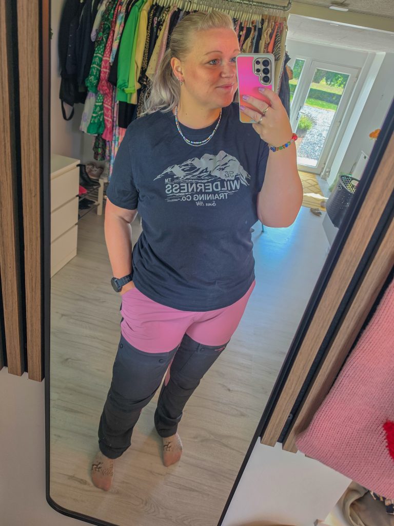 Woman trying on plus-size hiking trousers and outdoor clothing at home.